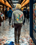 Model wearing custom hand-painted denim jacket featuring colorful hummingbird and floral artwork.